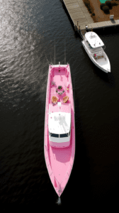 A pink boat with two white boats in the water.